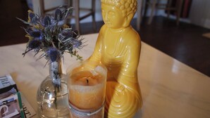 A Buddha statue, a vase with dried flowers, and a candle on a table. - The Establishment (Atl)