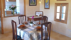 Comedor con una mesa dispuesta para cuatro personas, sillas alrededor y una cocina visible a través de un vano abierto.