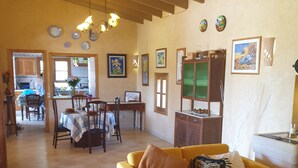 Amplia sala de estar con un sofá amarillo, una mesa de centro de vidrio y un comedor con sillas y mesa de madera.