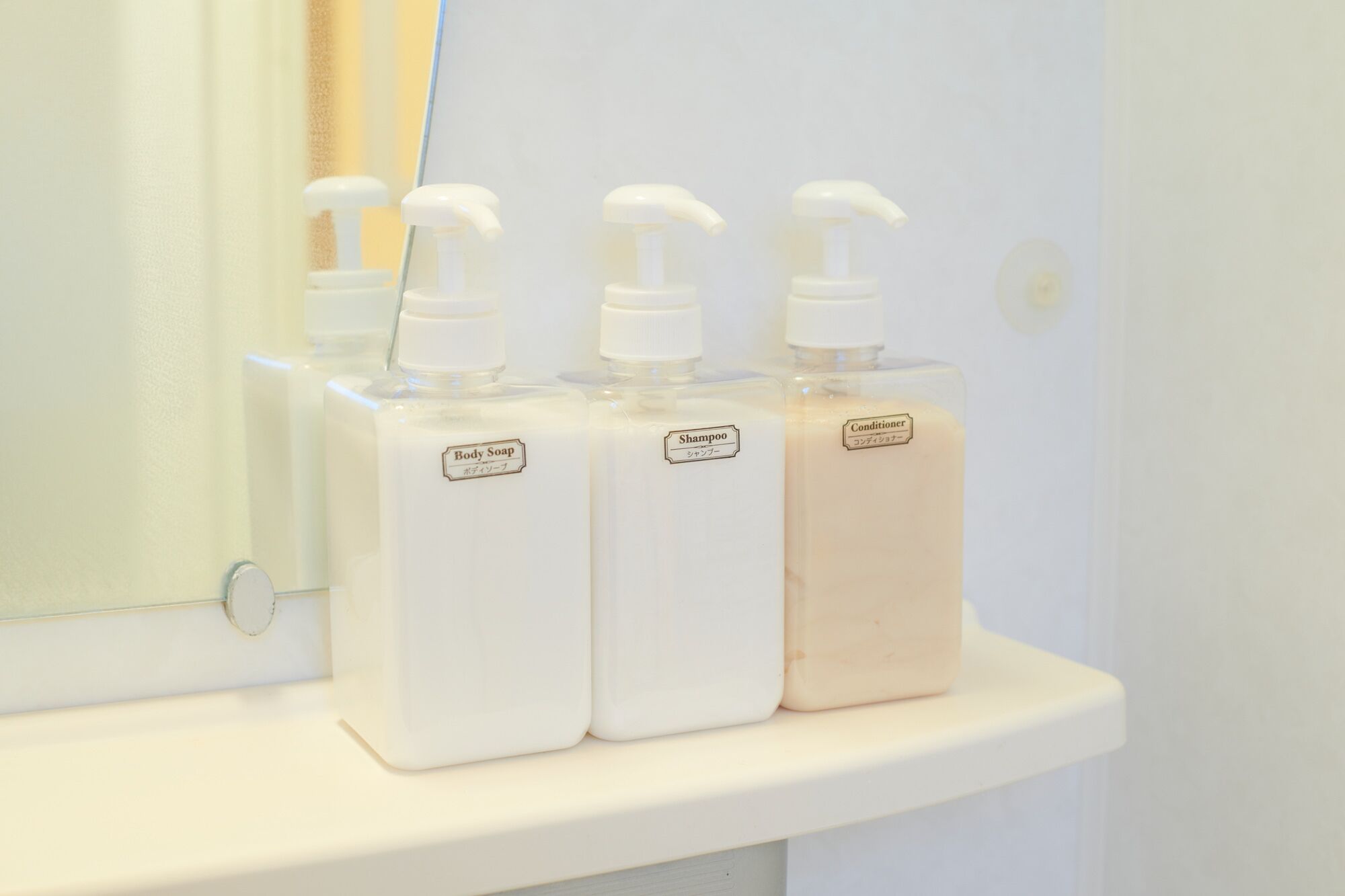 Three bottles of body soap and conditioner on a white shelf.
