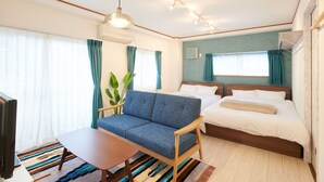 A hotel room with a sofa, two beds, a TV, a plant, and a colorful striped rug. - Ryoushi Minpaku CHOUTA (Awaji)