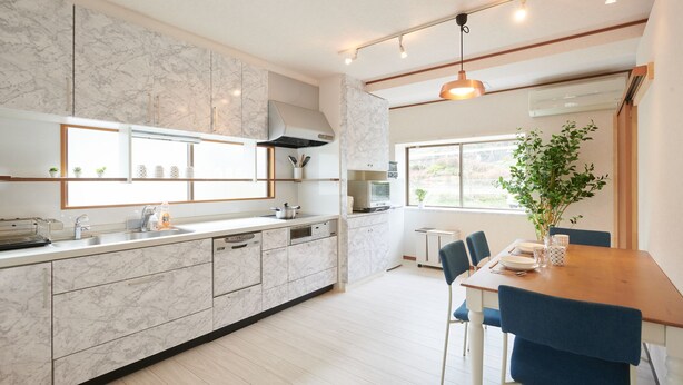 A modern kitchen with marble countertops, a built-in oven, and a dining area with a table and chairs. - Ryoushi Minpaku CHOUTA (Awaji)