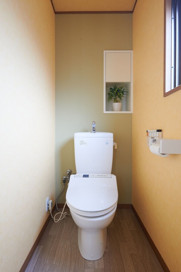 Un baño pequeño con un inodoro blanco, un estante con una planta en maceta y un porta papel higiénico en la pared.
