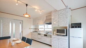 A modern kitchen with marble countertops, a built-in oven, microwave, and refrigerator. There is a dining area with a wooden table and blue chairs. - Ryoushi Minpaku CHOUTA (Awaji)