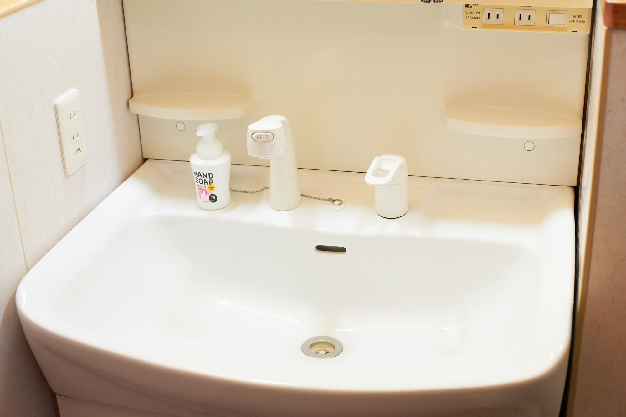A white sink with a hand soap dispenser, a soap bottle, and a faucet.
