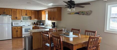 A kitchen with wooden cabinets, a dining table, chairs, a ceiling fan, and a window.