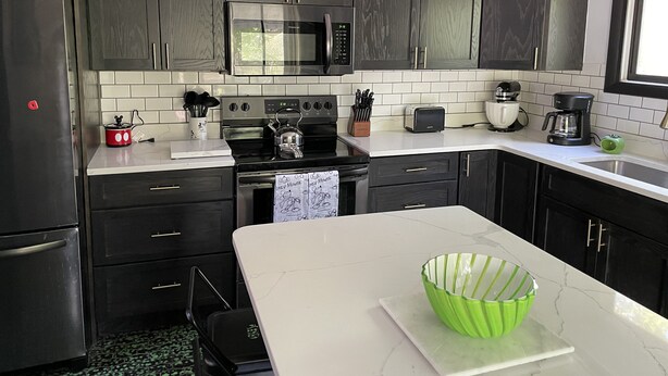 Una cocina moderna con armarios oscuros, un refrigerador de acero inoxidable, un microondas, una estufa y una cafetera.