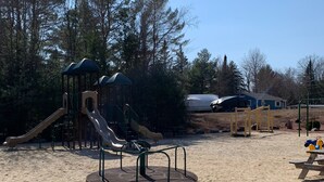 Un parque infantil con toboganes y un carrusel, rodeado de árboles y una zona de arena.