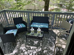 A covered outdoor seating area with wicker furniture, a patterned rug, and a glass coffee table.