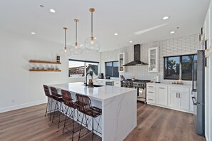 A modern kitchen with white cabinetry, a large island with bar stools, and a stainless steel range hood. - * Ocean view rooftop* Peloton* Modern & New (Dana Point)