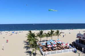 A beach with a fenced area containing tables and umbrellas, palm trees, and a clear view of the ocean. - Spacious Home Ready for your memories(2 blocks to beach, downtown and train) (Point Pleasant Beach)