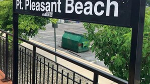 Schild mit der Aufschrift 'Pt. Pleasant Beach', ein Parkplatz und Grünfläche im Hintergrund.