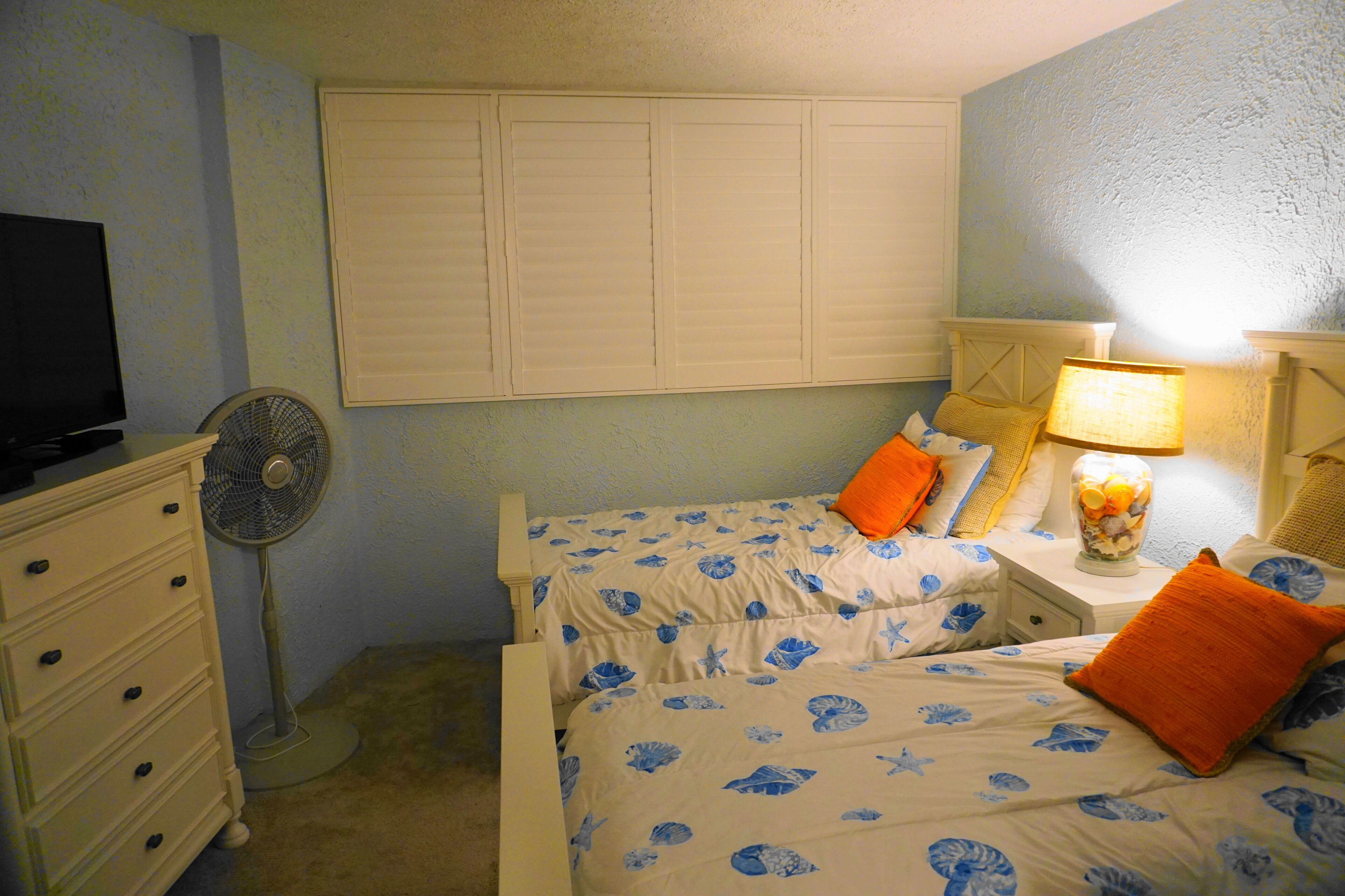 Een slaapkamer met een bed, een dressoir, een ventilator en een lamp.