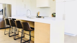 Cocina moderna con armarios blancos, refrigerador de acero inoxidable, una isla central con taburetes de bar e iluminación colgante.