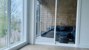 Una habitación con un amplio ventanal corredera que da a un espacio exterior, piso de madera y alfombra de cuero de vaca.
