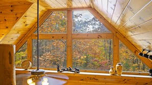 Uma cabana de madeira com telhado inclinado e grandes janelas que oferecem vista para árvores de outono.