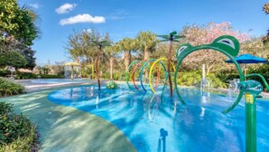 Un parque acuático con piscina, toboganes coloridos y una fuente con forma de tiburón.