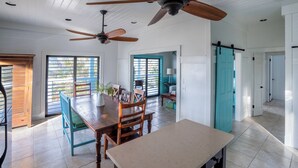 Une cuisine spacieuse dotée de deux ventilateurs de plafond, un coin repas avec des chaises en bois et une grande fenêtre donnant sur un paysage verdoyant.