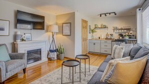 A living room with a fireplace, sofa, coffee table, and a kitchen in the background.