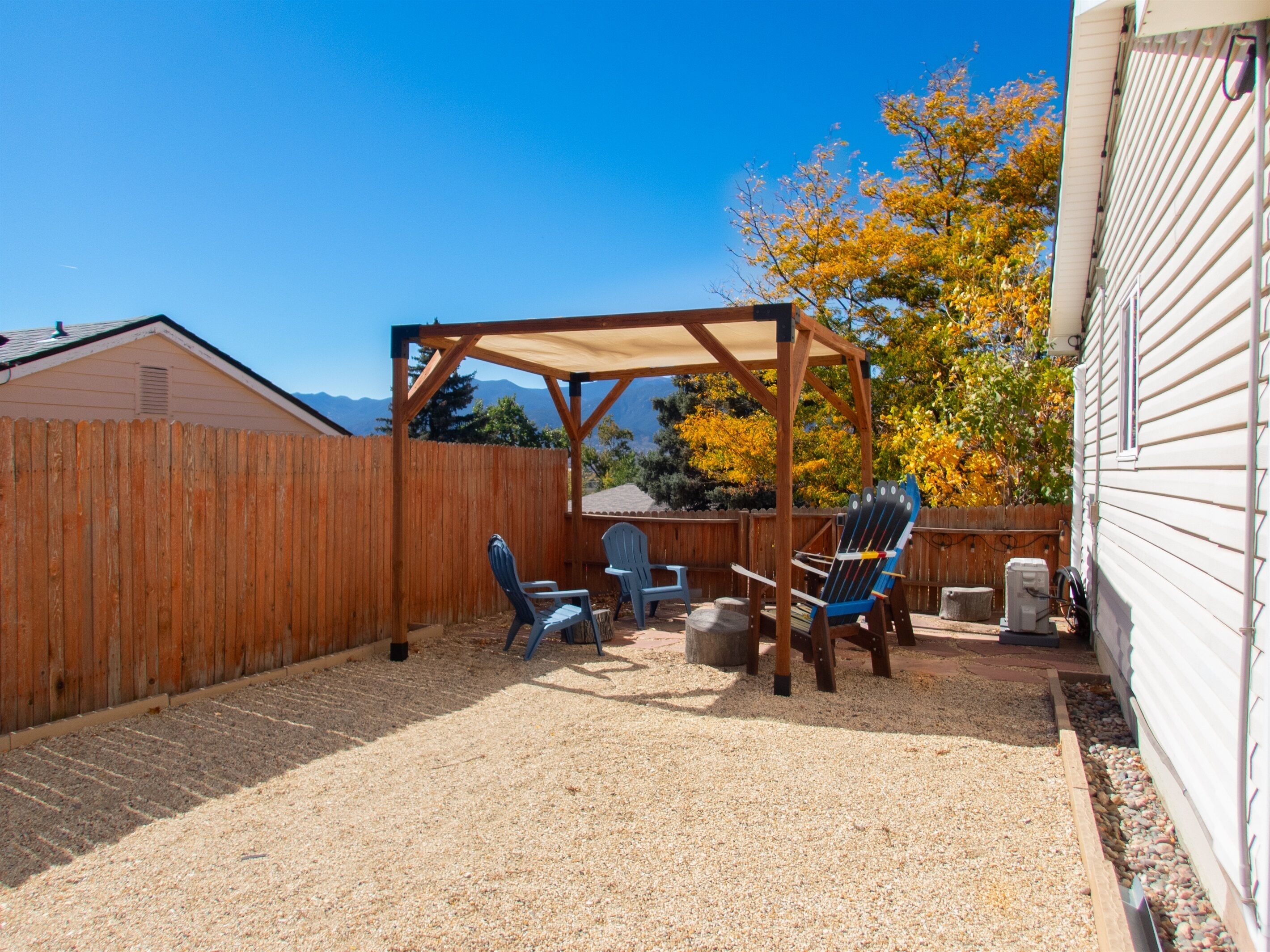 Un patio trasero con cerco de madera, pérgola y mobiliario exterior.