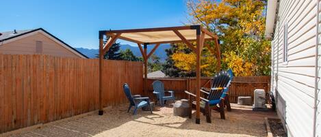 Un patio trasero con cerco de madera, pérgola y mobiliario exterior.
