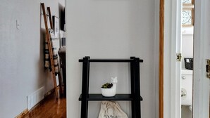 A hallway with a wooden floor, a black shelf with a white bag, and a framed picture on the wall.