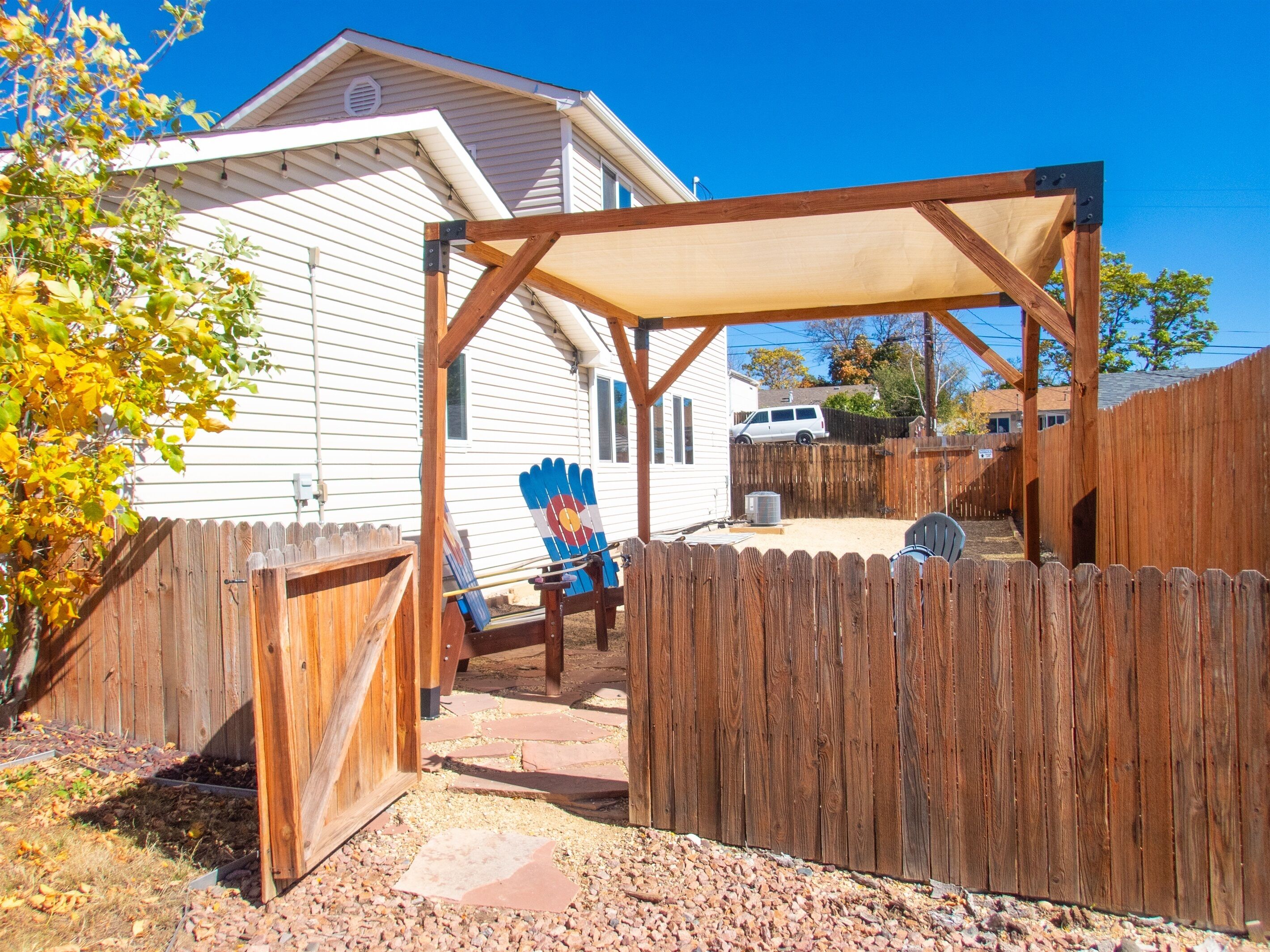 A backyard with a wooden fence, a covered patio area, and a blue flag.