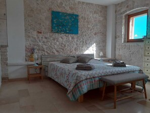 Ein Schlafzimmer mit einer Steinwand, einem Bett mit floralem Überwurf, einer Bank, einem Nachttisch und einem Fenster mit Blick.