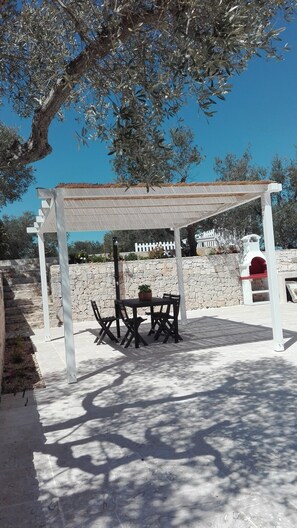 Ein überdachter Außenbereich mit Tisch und Stühlen, einer Steinwand und einer weißen Pergola.