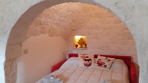 Une chambre avec une arche en pierre, un lit recouvert d’une courtepointe à motifs, deux oreillers et une petite table avec une lampe.