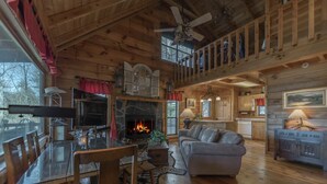 A cozy cabin interior with a stone fireplace, wooden dining table, and a loft area with a balcony. - Private pet-friendly Aska Adventure Area getaway with gorgeous views! (Blue Ridge)