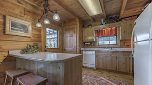 A wooden cabin interior with a kitchen area, wooden bar stools, a refrigerator, and a patterned rug. - Private pet-friendly Aska Adventure Area getaway with gorgeous views! (Blue Ridge)