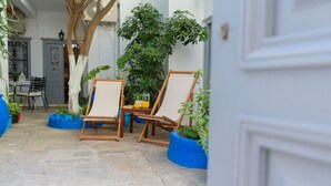 A stone-floored patio with two wooden chairs and a table, surrounded by blue planters and a large green plant. - Hydra's Pearl - Blue Pearl (Hydra)