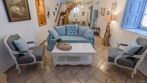 A living room with a blue sofa, two armchairs, a white coffee table, and a staircase leading to another room. - Hydra's Pearl - Blue Pearl (Hydra)