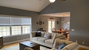Un salon avec un canapé beige, une table basse et un coin repas comprenant une table et des chaises en bois.