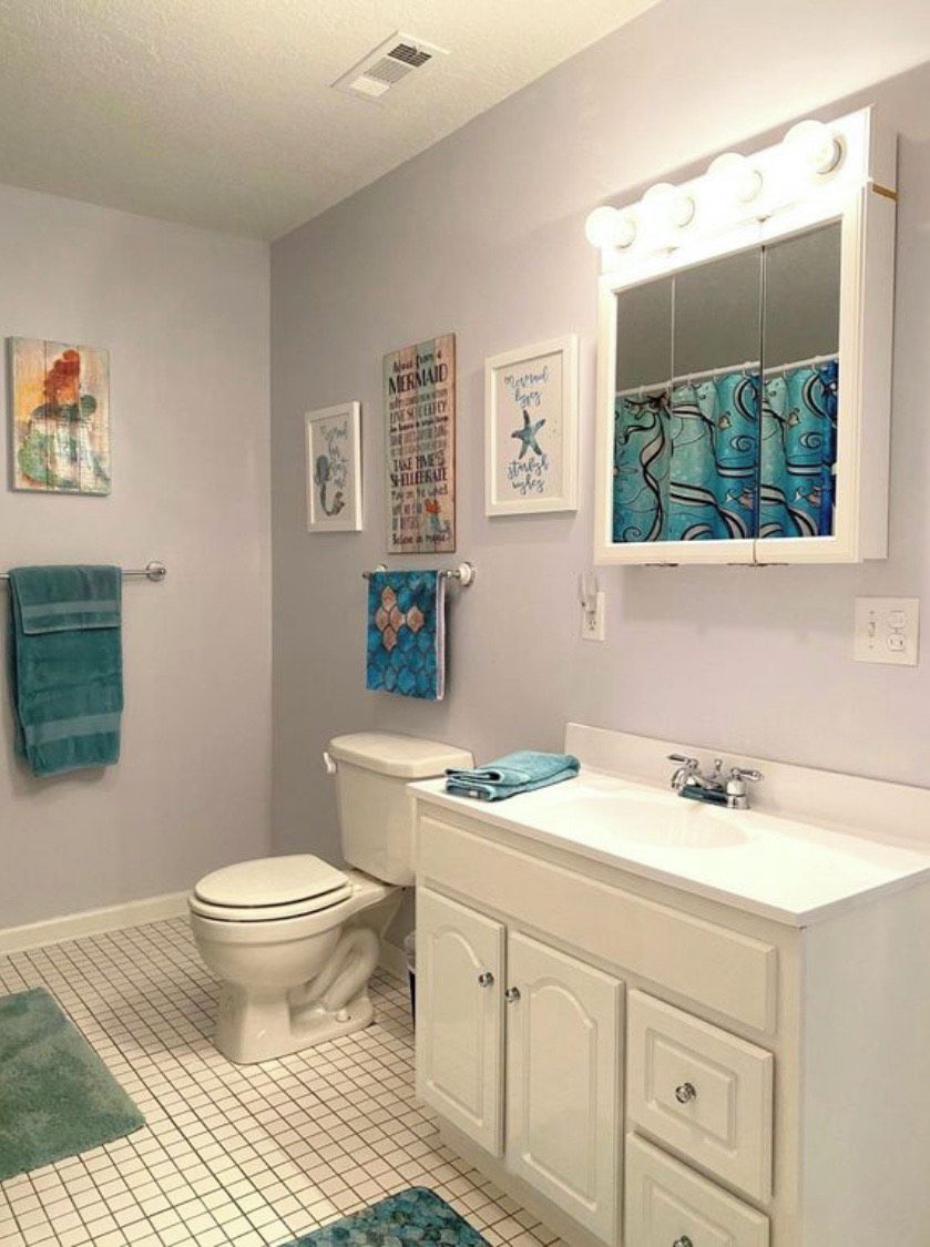Un baño con inodoro, lavamanos y armario, que presenta un suelo con diseño de cuadrícula y una obra de arte colgada en la pared.