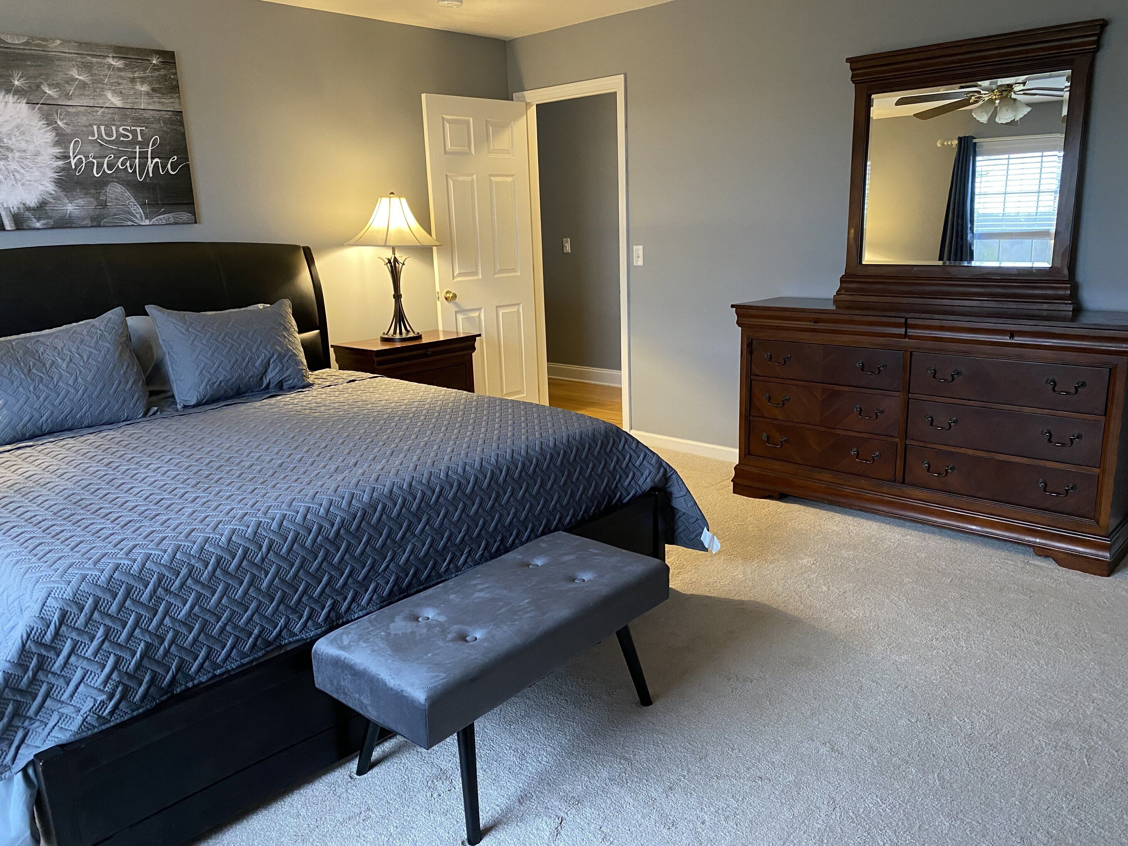 A bedroom with a bed, a bench, a dresser, a mirror, and a wall with a motivational quote.