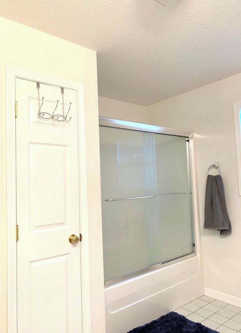 A bathroom with a white door, a shower with a glass door, and a towel hanging on a hook.
