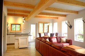 Relax in a spacious seating area with a leather sofa and dining table, surrounded by large windows and a wooden ceiling with exposed beams.