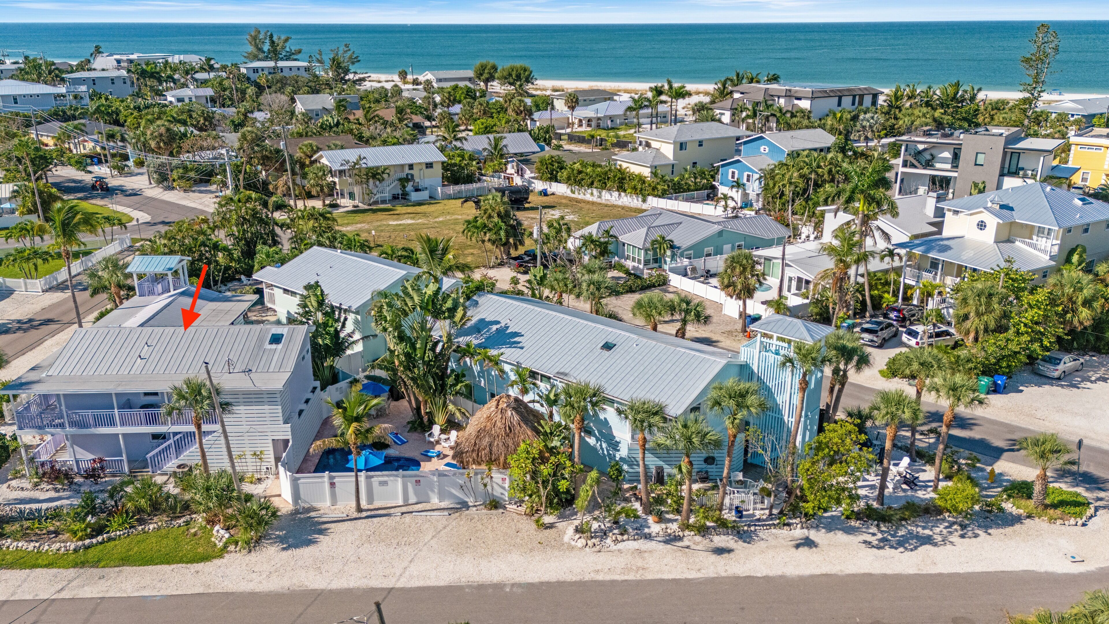 An aerial view of a coastal residential area with houses, a beach, and a large building with a pool.