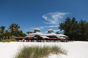 A beachfront restaurant with outdoor seating and a white building with a peaked roof.