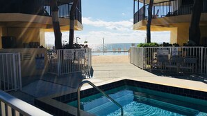A pool area with a view of the ocean, surrounded by balconies and a fenced pool. - KG Arrive any day, pool on beach, full Kitchen, W/D, Parking, Docks, balcony,  (Marathon)