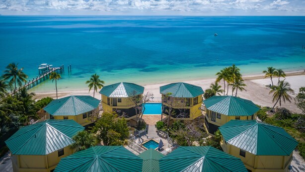 A resort with multiple green-roofed buildings, a swimming pool, and a beach with clear blue water. - KG Arrive any day, pool on beach, full Kitchen, W/D, Parking, Docks, balcony,  (Marathon)