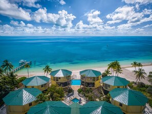 A resort with multiple green-roofed buildings, a swimming pool, and a beach with clear blue water.