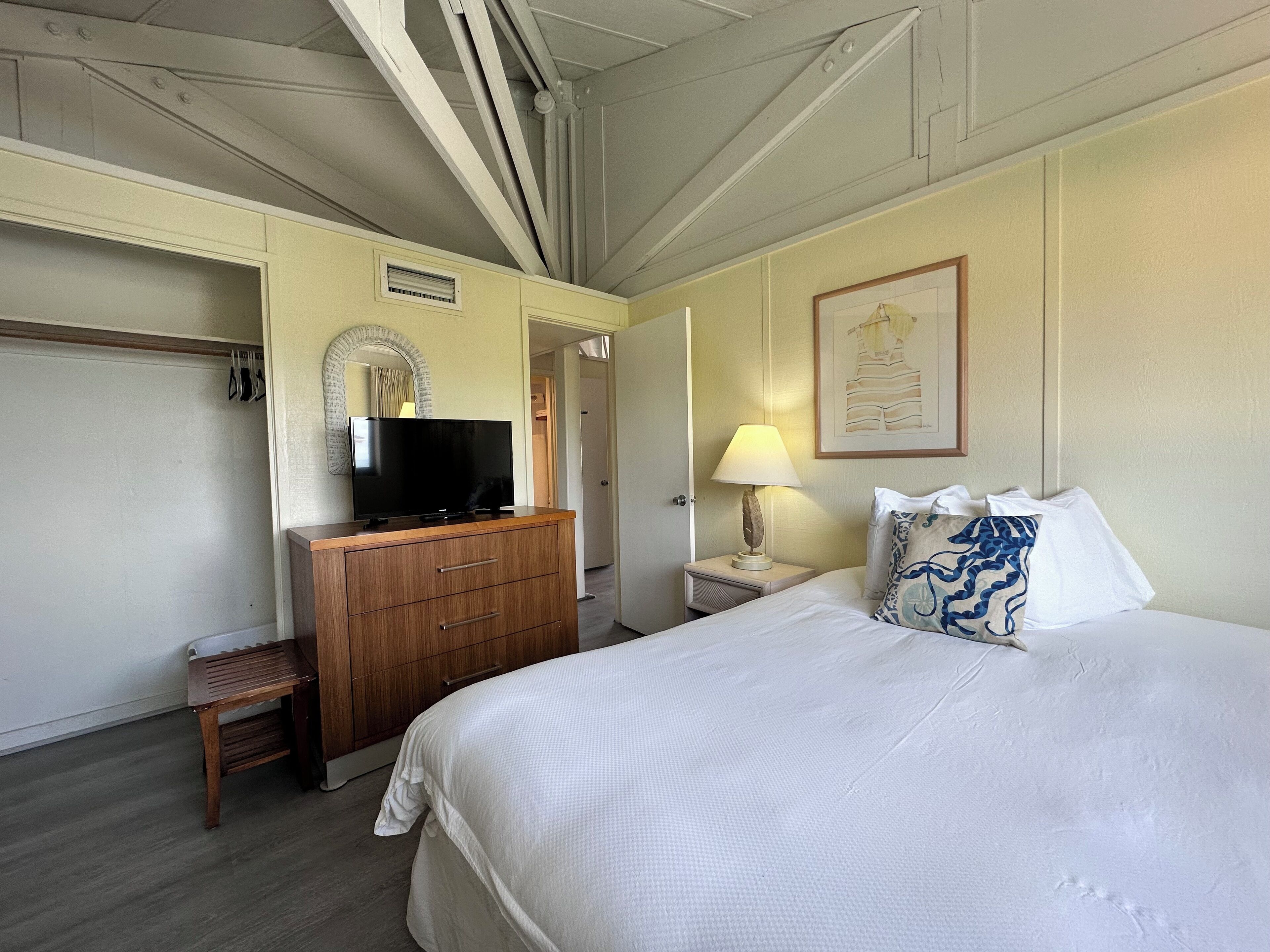 A hotel room with a bed, a TV on a wooden dresser, a lamp, and a framed picture on the wall.