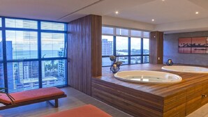 A modern bathroom with a large bathtub, two sun loungers, and a view of the city through large windows. - TIME BUILDING - BEST LOCATION IN THE CITY (maceio)