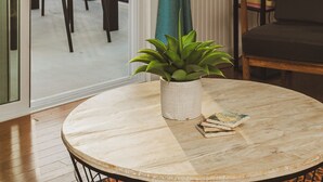 A room with a view of palm trees and a balcony. There is a round table with a plant and books, a black chair, and a tall black bookshelf. - SURFS UP - UP STAIRS UNIT (Bradenton Beach)