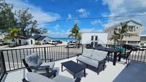 A balcony with outdoor furniture, a view of the beach, and a building with a pool in the background. - SURFS UP - UP STAIRS UNIT (Bradenton Beach)