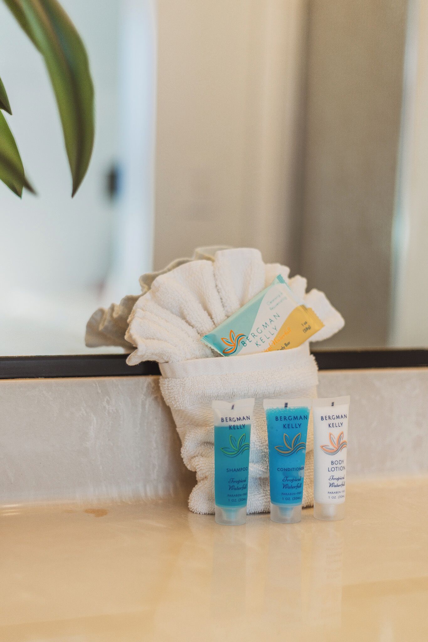 Une salle de bain avec une serviette blanche, trois produits de la marque Bergman Kelly et une plante en arrière-plan.