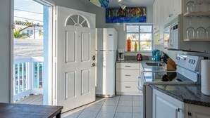 A kitchen with white cabinets, a refrigerator, a coffee maker, and a window with a view of the outside. - SURFS UP - UP STAIRS UNIT (Bradenton Beach)